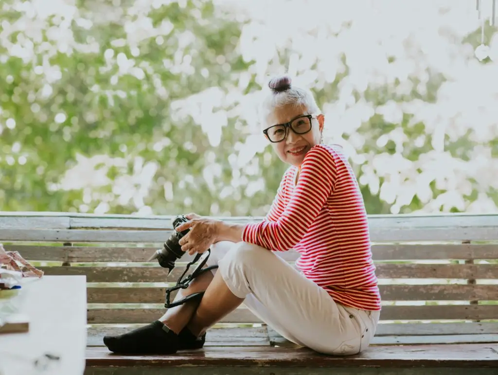 An older woman sitting on a bench holding a camera