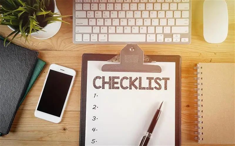 A smartphone, note pads and checklist at a computer desk