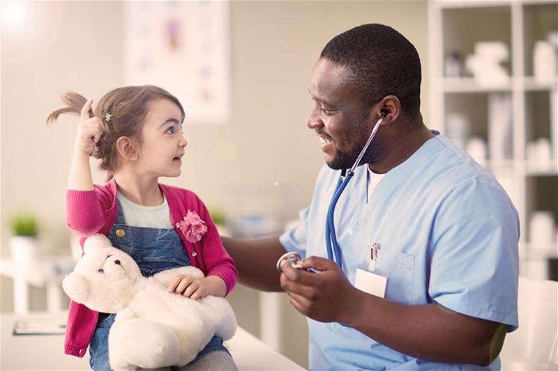 Little girl with teddy bear telling her doctor a story