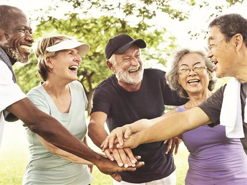 A diverse group of older people huddle and stack hands together in a circle