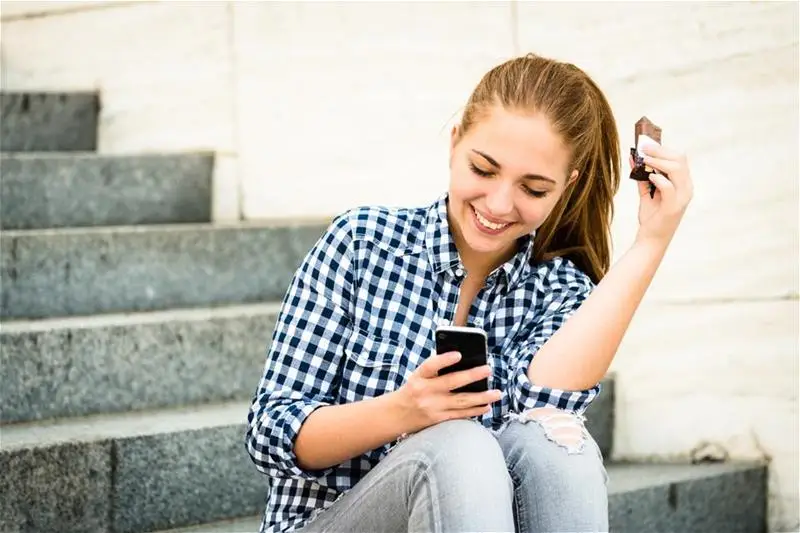 A woman eating a chocolate bar looking at her phone sitting on steps
