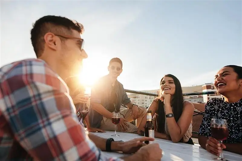 A group of friends sit on a rooftop drinking wine and beer