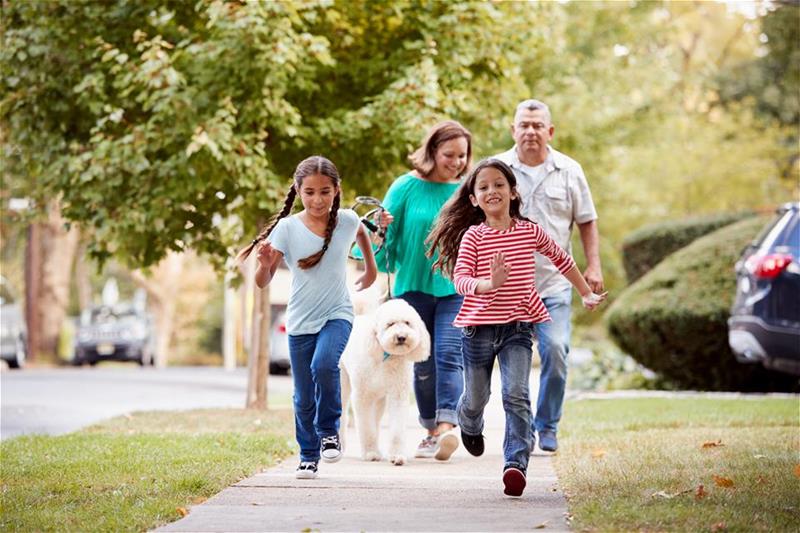 Kids run on the sidewalk while their parents, walking the dog, follow close behind
