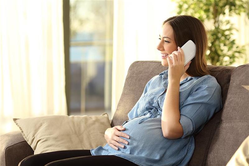 Pregnant woman sits on the couch smiling while talking on the phone