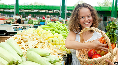 Una joven en el mercado agrícola llenando su cesta de verduras