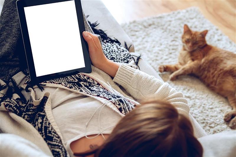 A woman lying next to a cat using a tablet