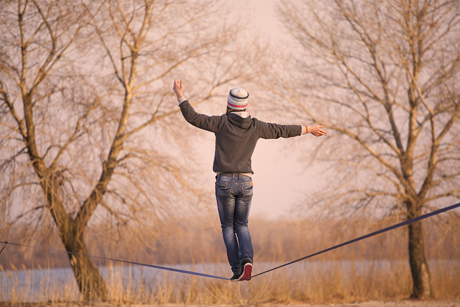 Young person balancing on a tightrope connected between trees