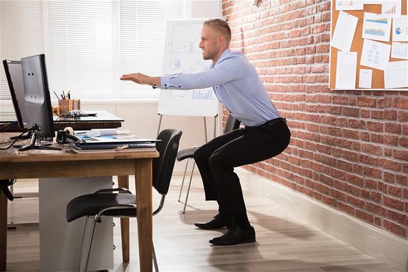 Man doing squats at his office desk
