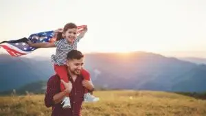A man holding a child on his shoulders holding an American flag in the air