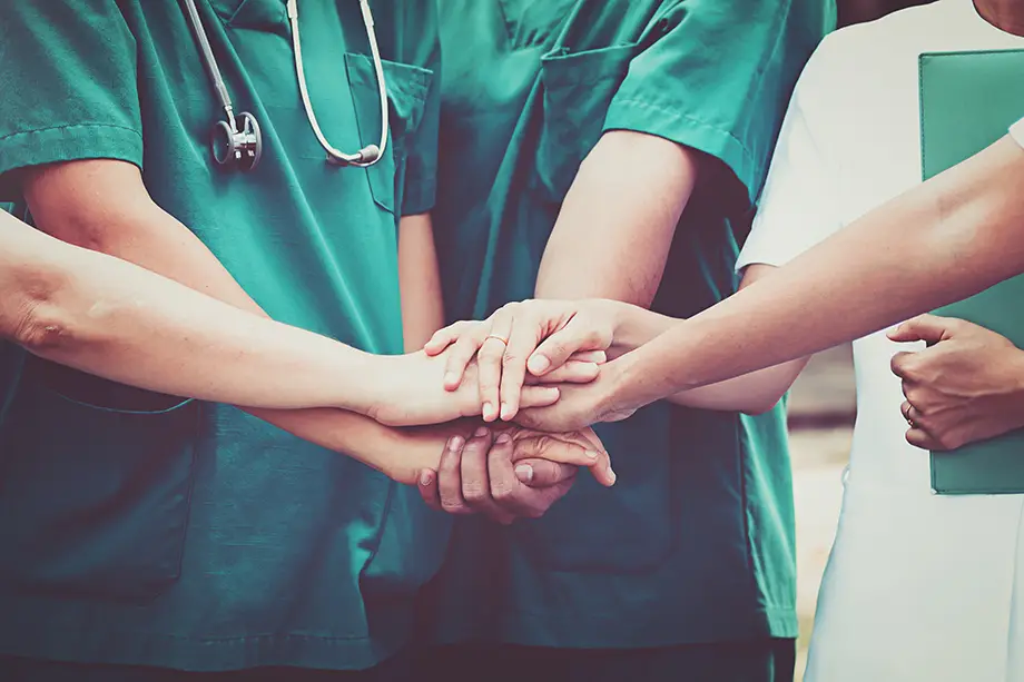 A group of health care professionals stand together with hands stacked in the middle