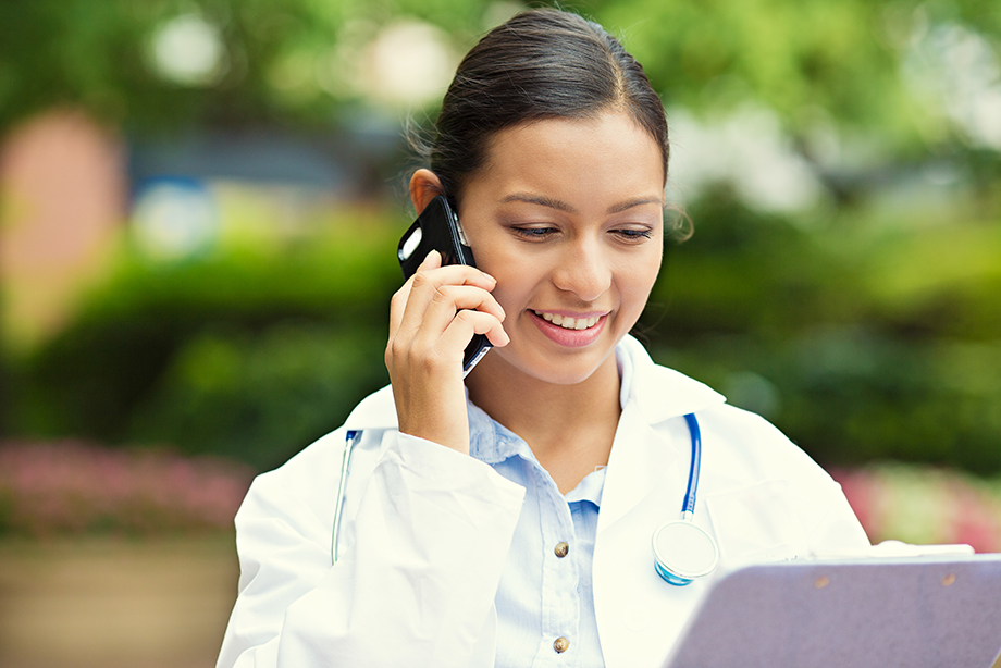 Young female doctor outside on phone with laptop open