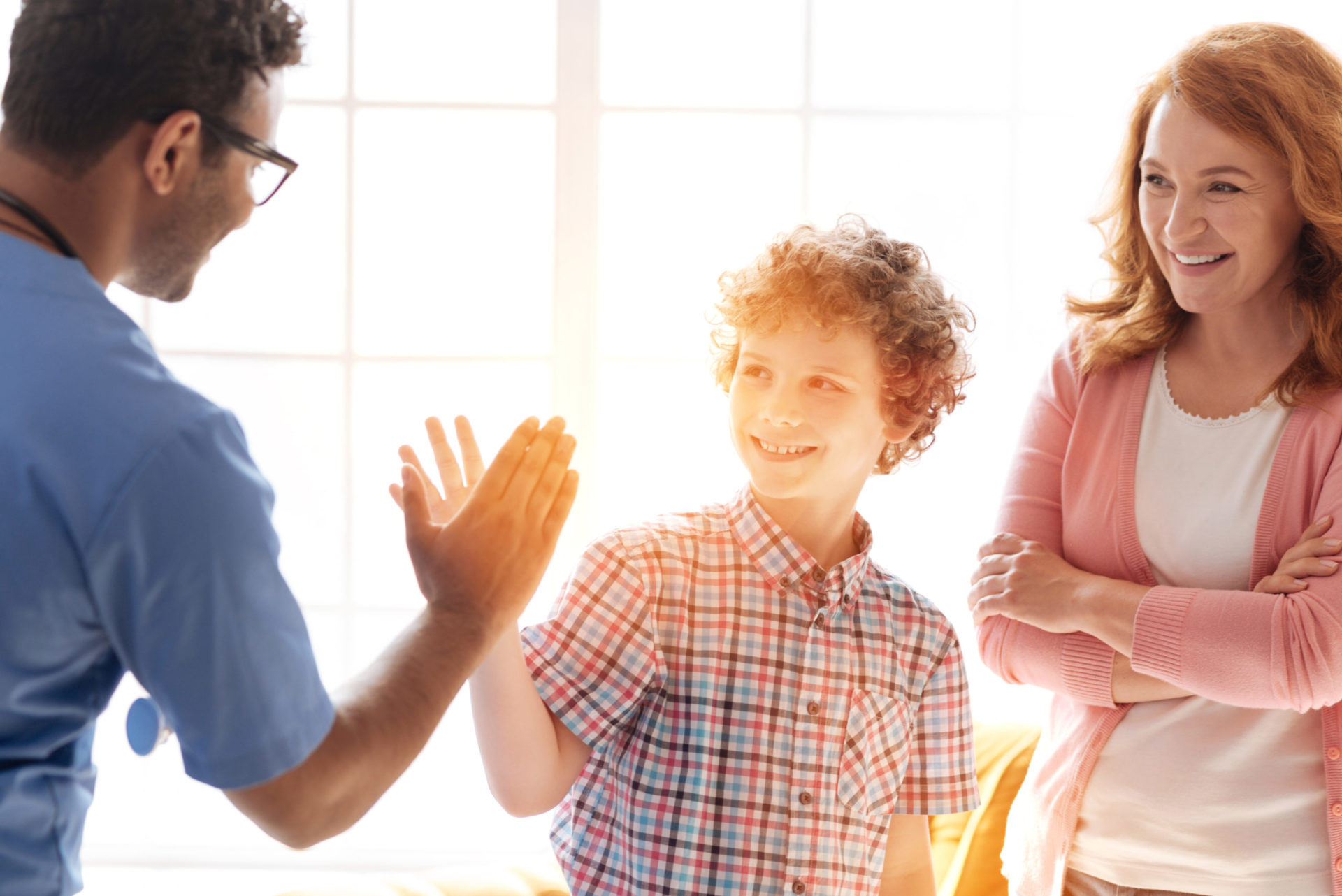 Kid high-fives his doctor at a doctor visit while his mom looks on, smiling