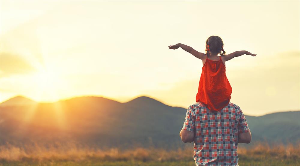 Little girl on dad's shoulders with arms spread out watching the sunrise