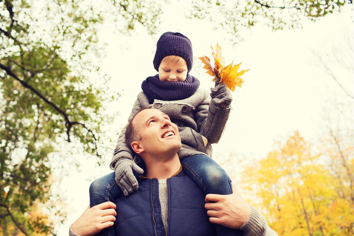 Papá con su hijo sobre los hombros sosteniendo un puñado de hojas de oro