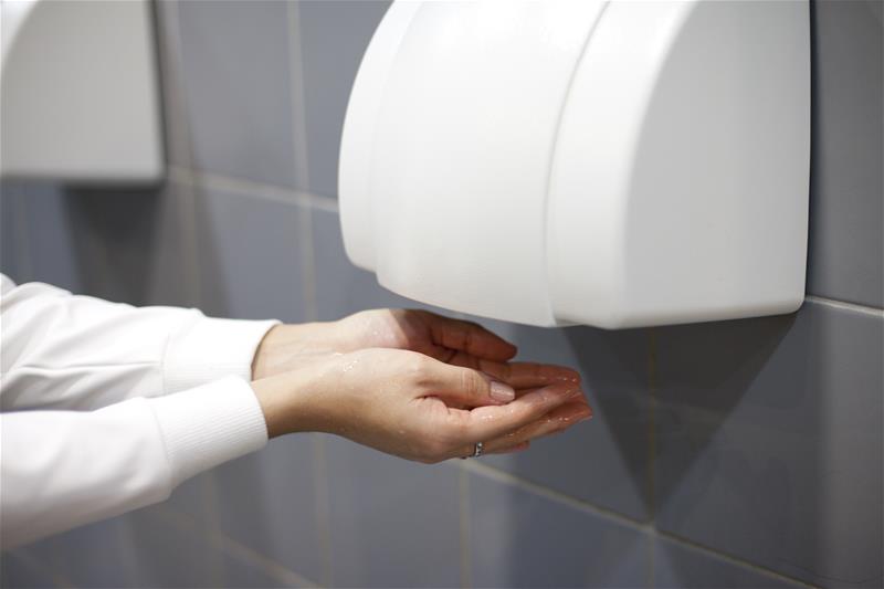 Mujer sujetando sus manos bajo un secador eléctrico en un baño
