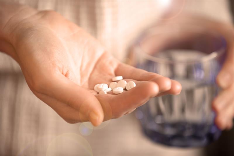 Woman holding a handful of pills in one hand and a glass of water in the other