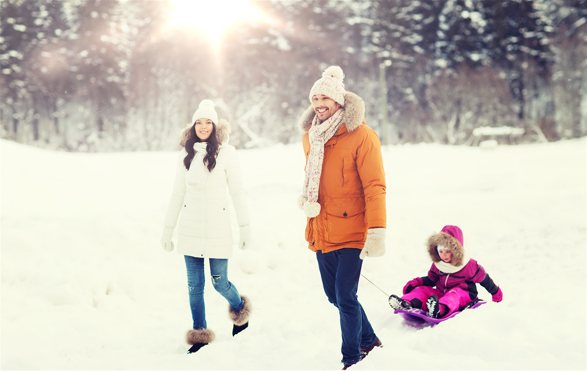 Young couple hiking through snow with dad pulling his daughter on a sled