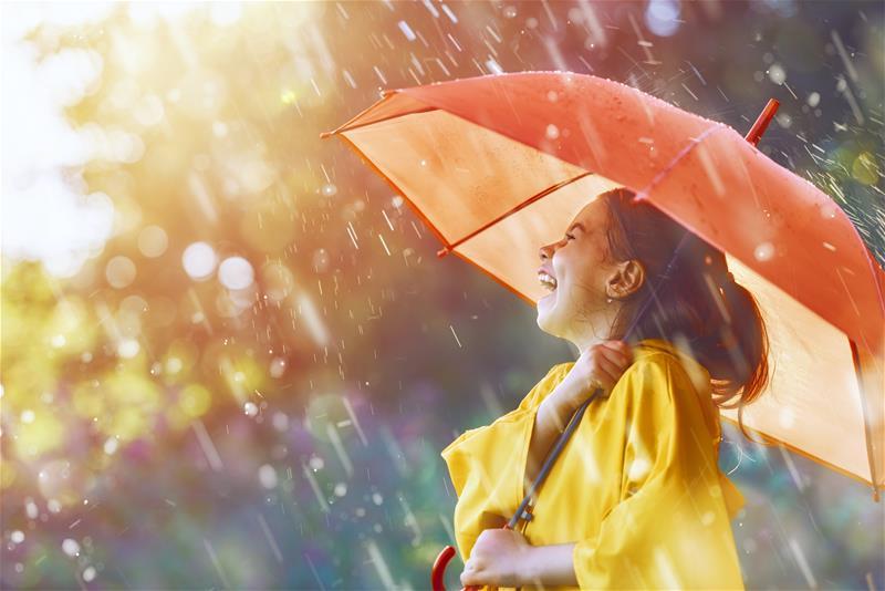 Smiling young girl walking in rain with an umbrella and raincoat