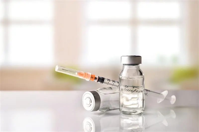 A vaccine vial and needle sit on a counter