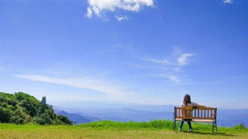 A woman sitting alone on a bench looking out over a hill