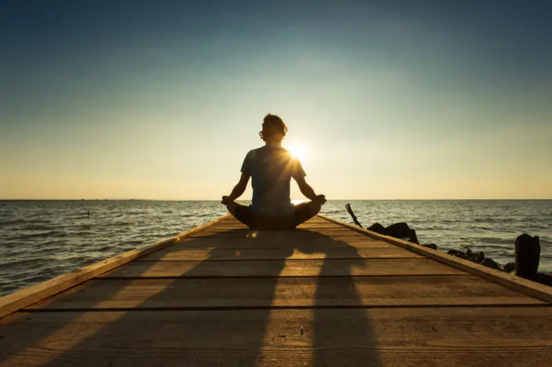 An Individual meditating on a lakeside pier at sunrise