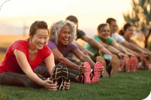 Group of people in athletic clothing stretching together on a grassy field outdoors.