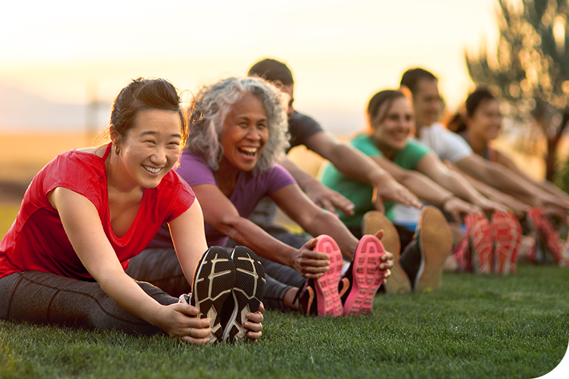 Group of people in athletic clothing stretching together on a grassy field outdoors.