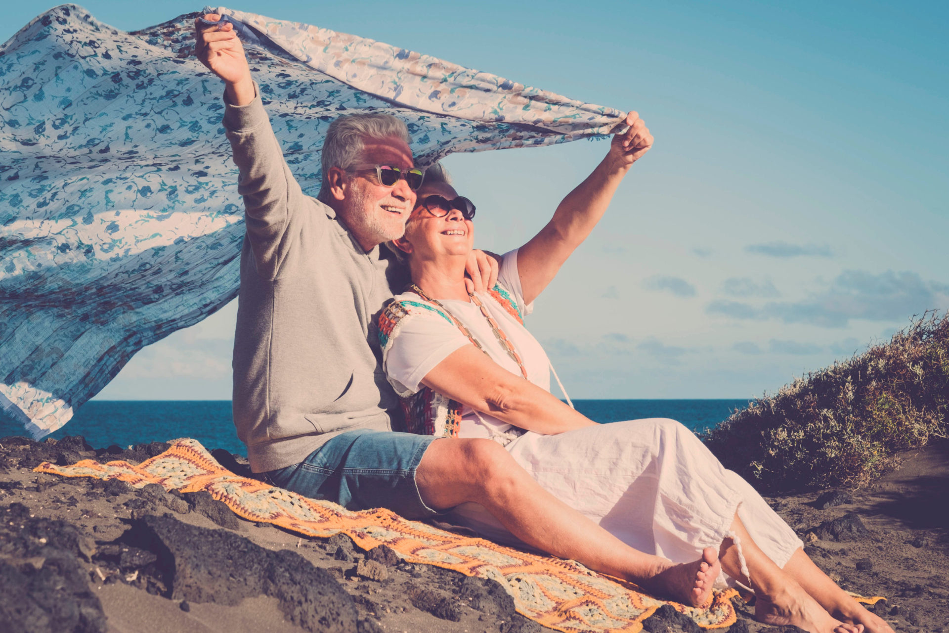 Couple using blanket to shield themselves from the sun while sitting on top of a hill