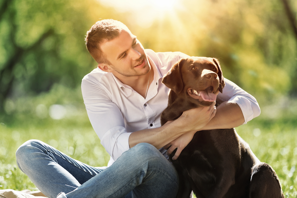 Young man sitting in the grass with his chocolate Labrador Retriever;
