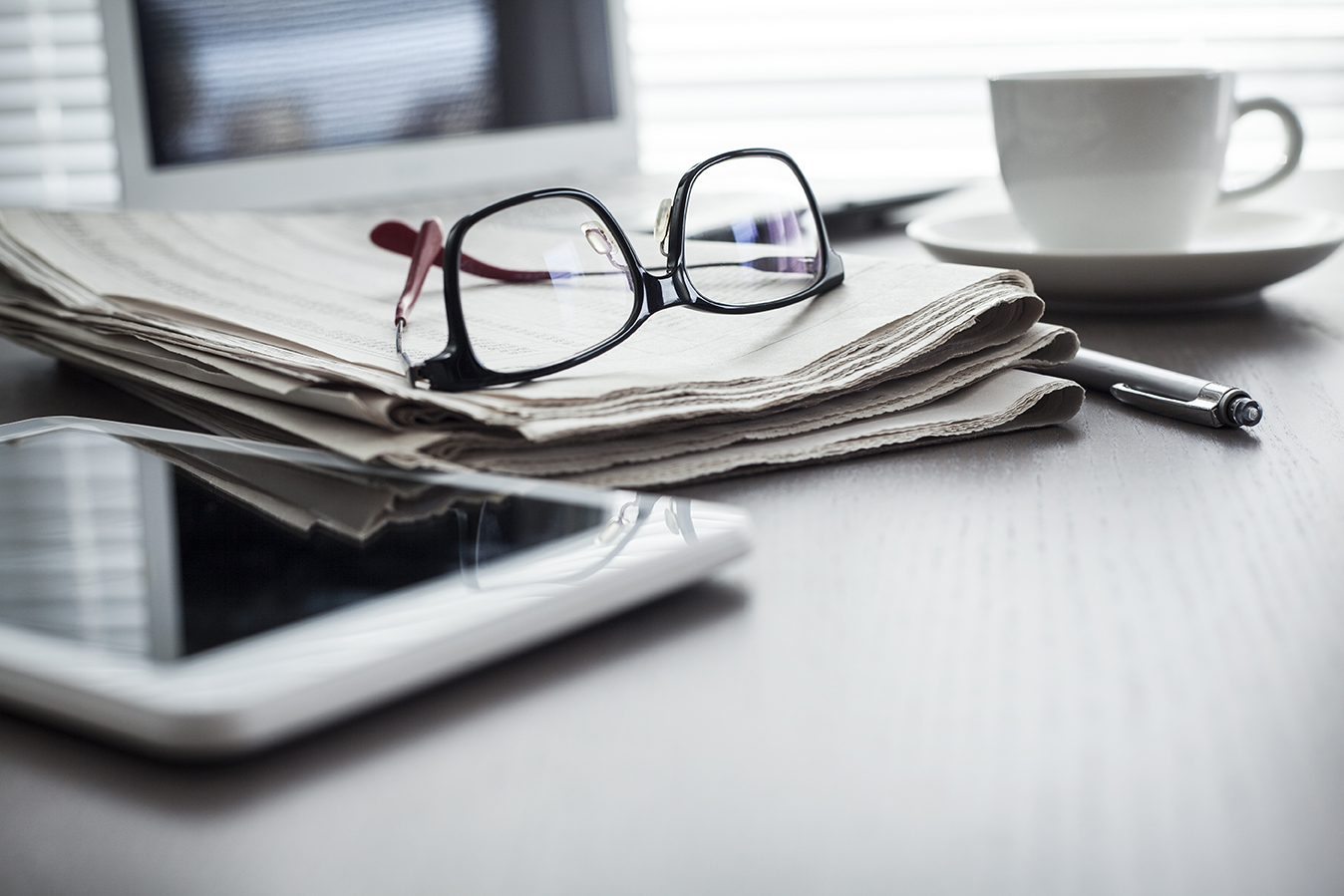 Eyeglasses and a newspaper next to a coffee cup