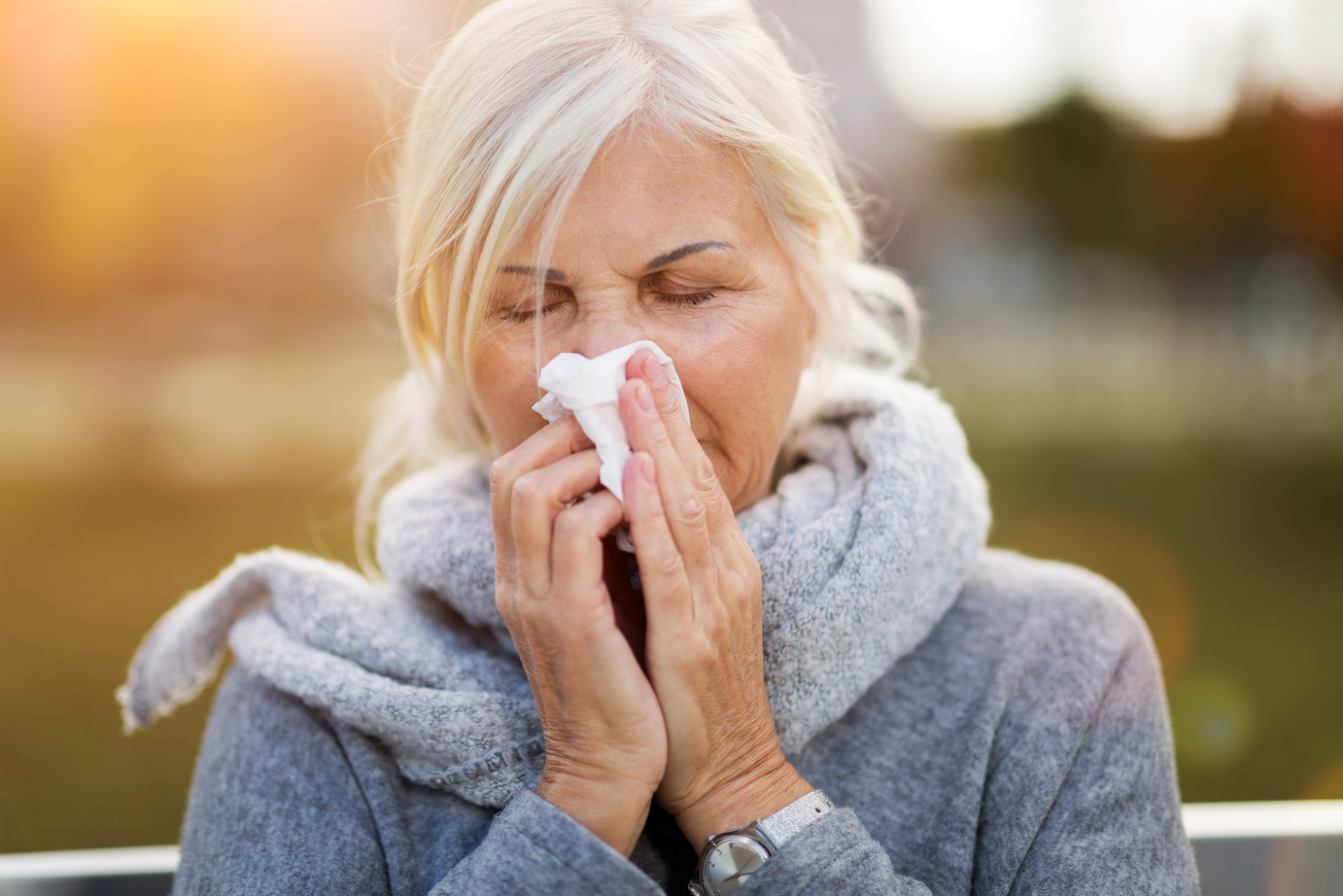 Mujer mayor estornudando en un pañuelo de papel mientras está al aire libre en otoño