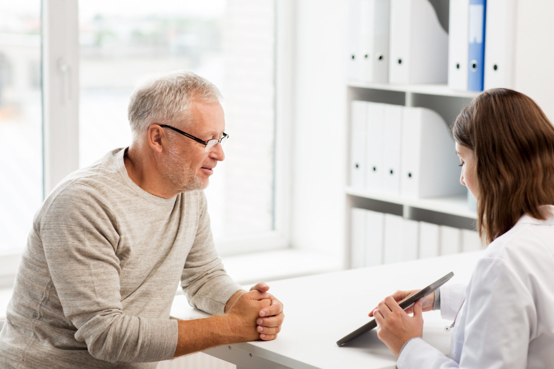 Un médico muestra a un paciente mayor algo en una tableta durante una consulta