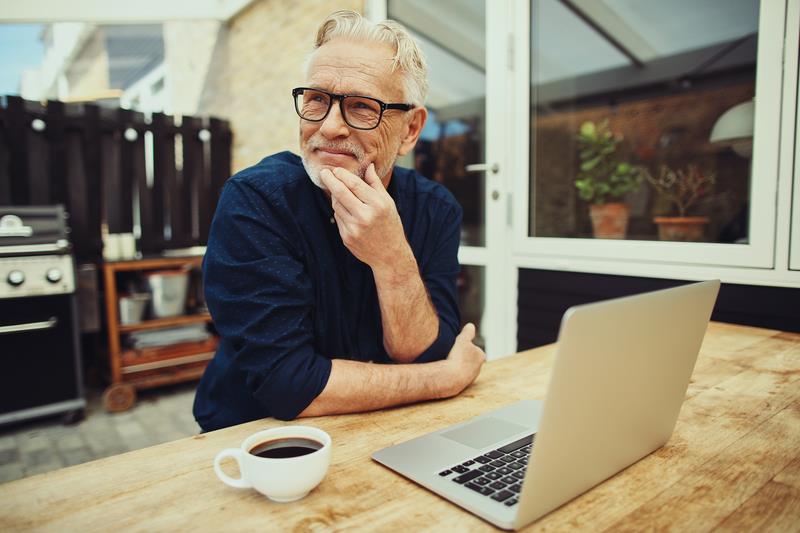 Senior man enjoying coffee on his deck with his laptop open