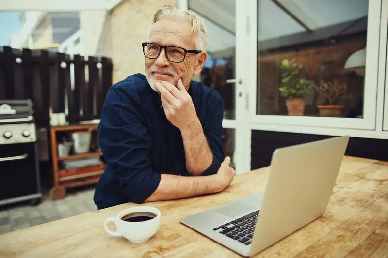 A senior man on a deck with a laptop and coffee