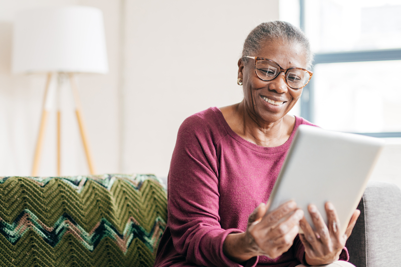 Older woman smiles looking at a tablet on her couch