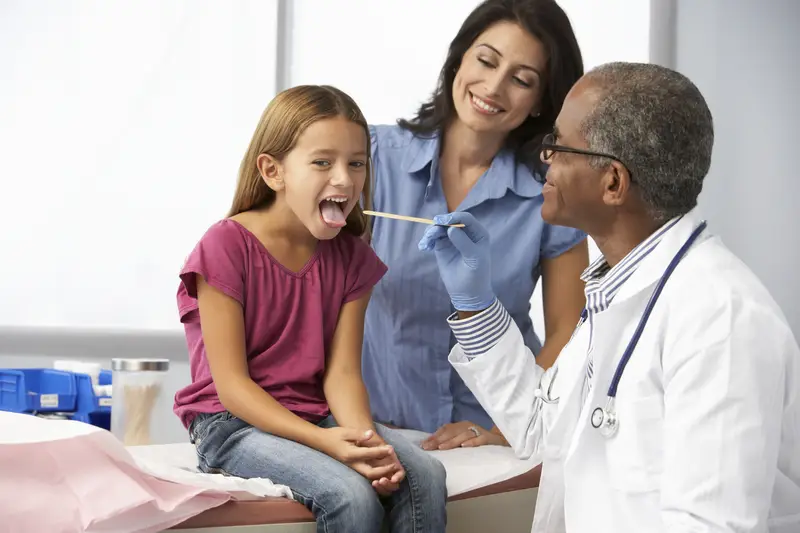 A doctor checks the back of a young girl's throat during a doctor visit