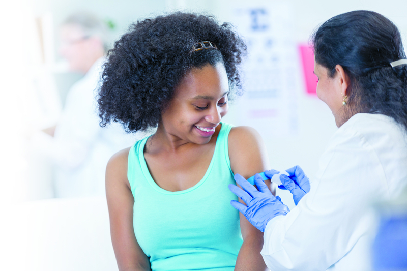 Una mujer coloca un vendaje en el brazo de una joven tras administrarle una vacuna