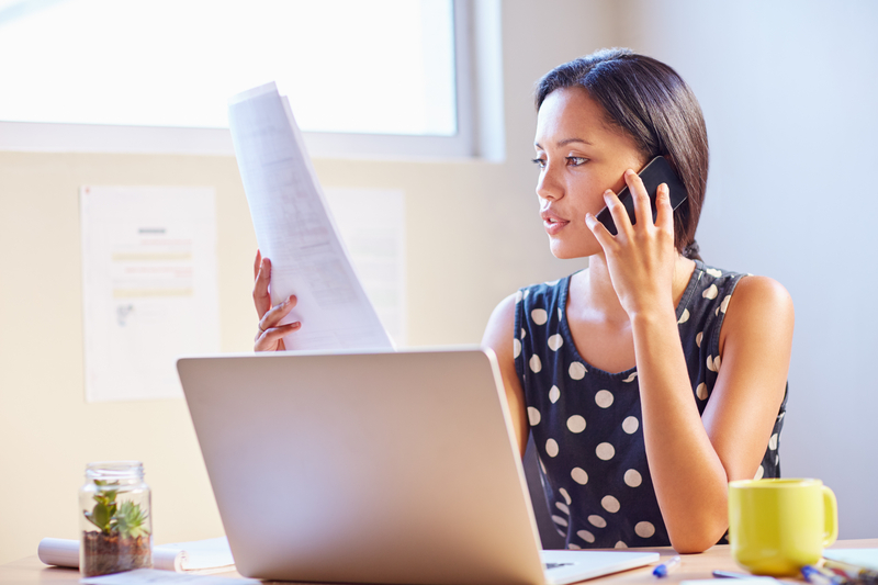 Woman looking at paperwork at her desk while talking on the phone