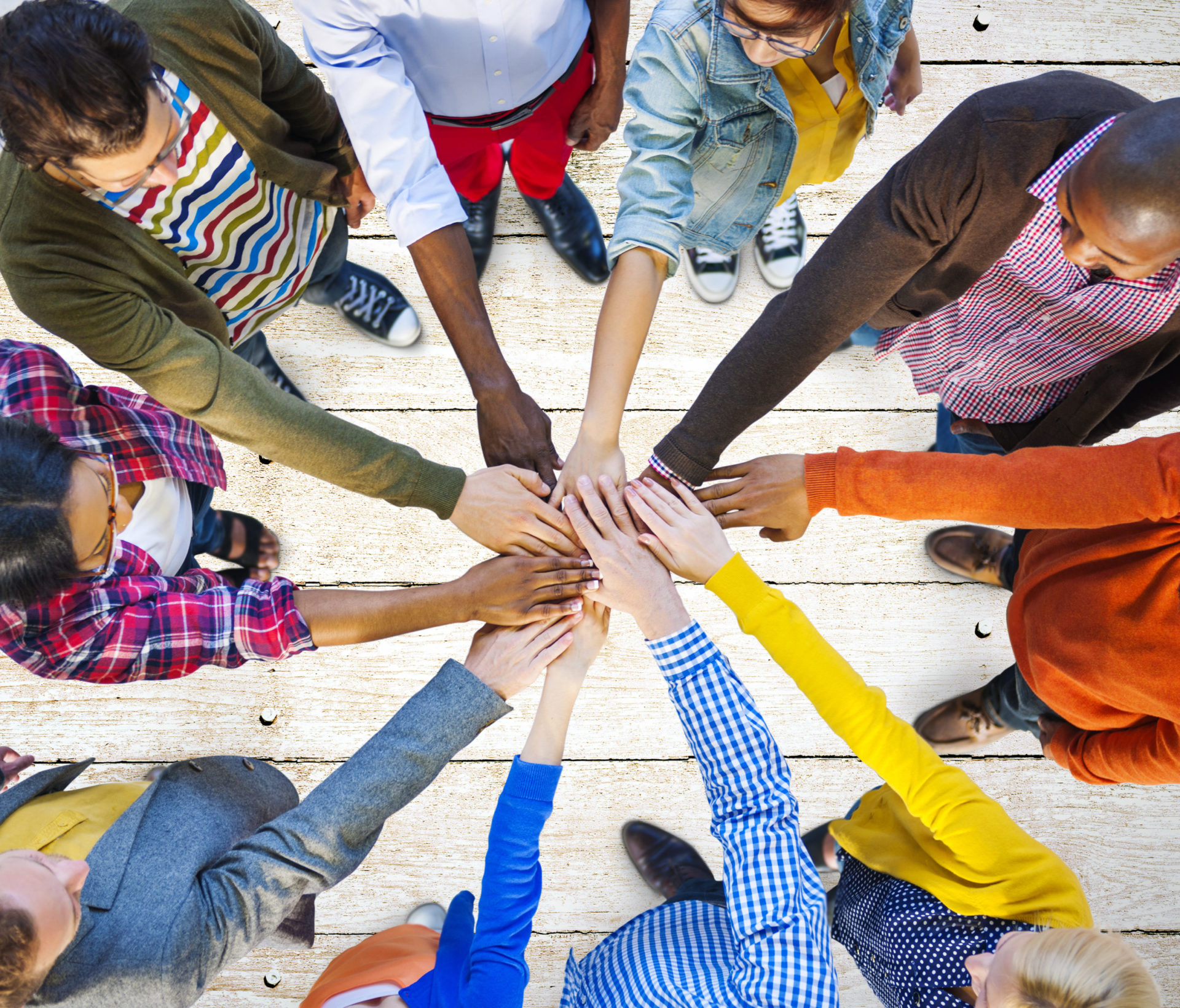 Diverse group of people circle up and stack hands as a team