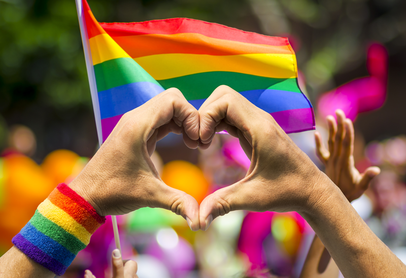 Rainbow flag at a pride parade with hands in shape of a heart in front