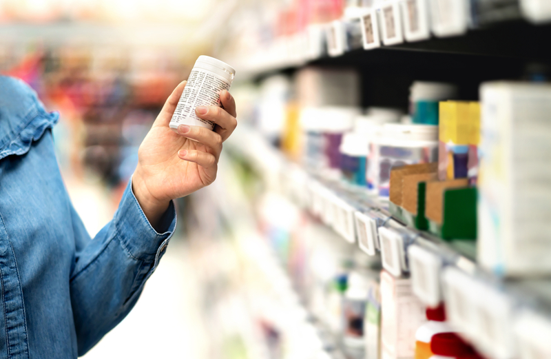 Una mujer lee la etiqueta de un frasco de pastillas en la farmacia