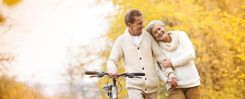 Older couple walk in autumn holding a bike