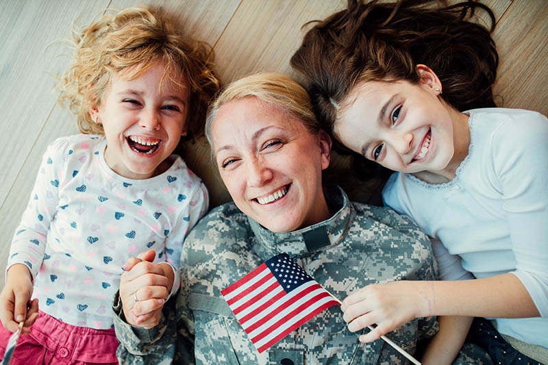 Mamá militar y sus hijas sonriendo mientras están tumbadas en el suelo
