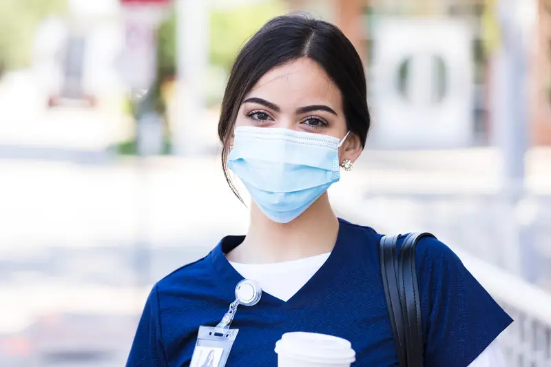 A healthcare professional wearing a face mask holding a cup of coffee