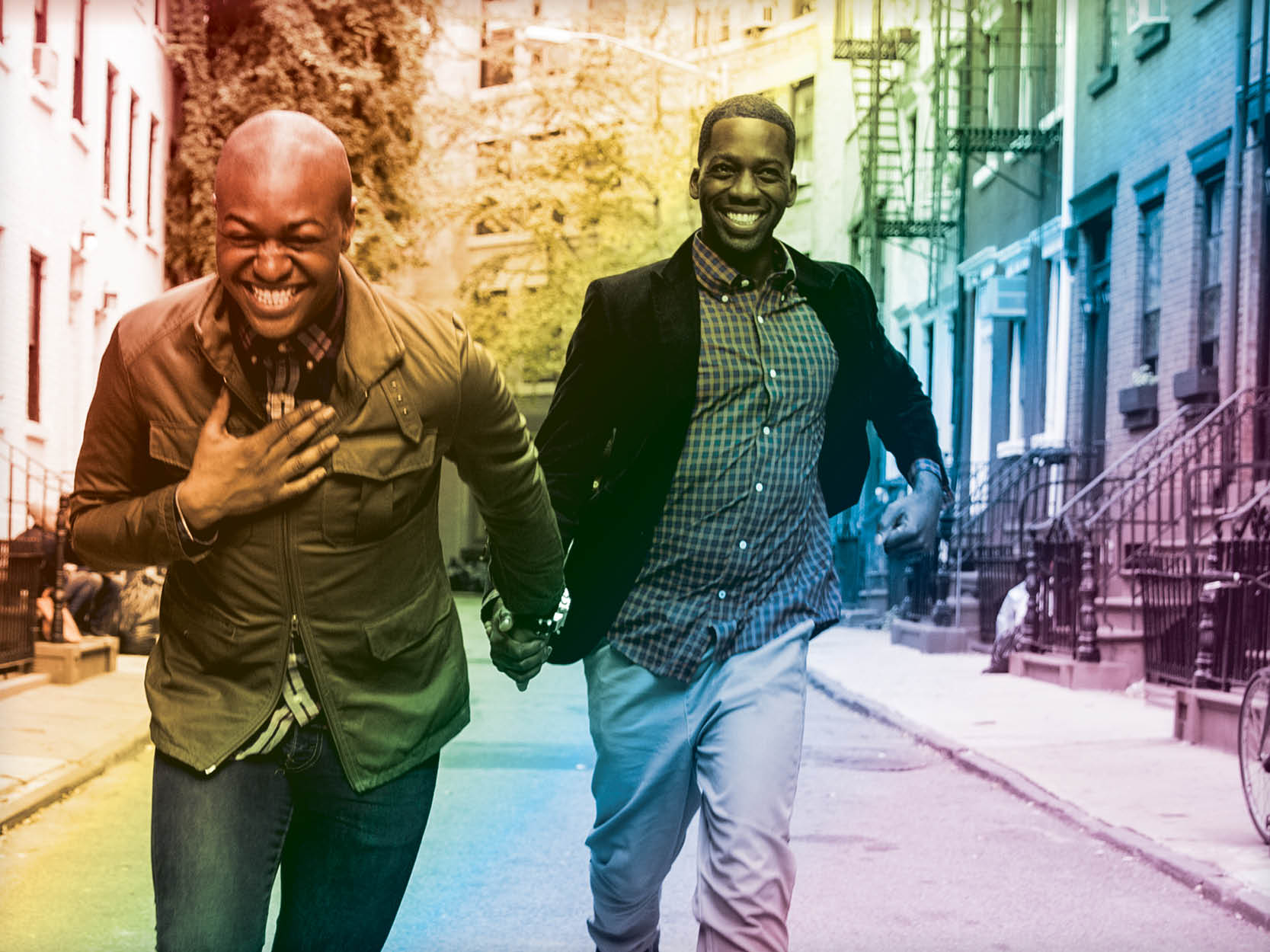 Two men holding hands and laughing as they walk down the street