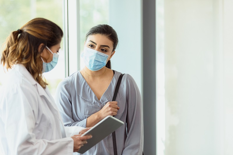 Doctor and patient standing in hall wearing masks and discussing her care