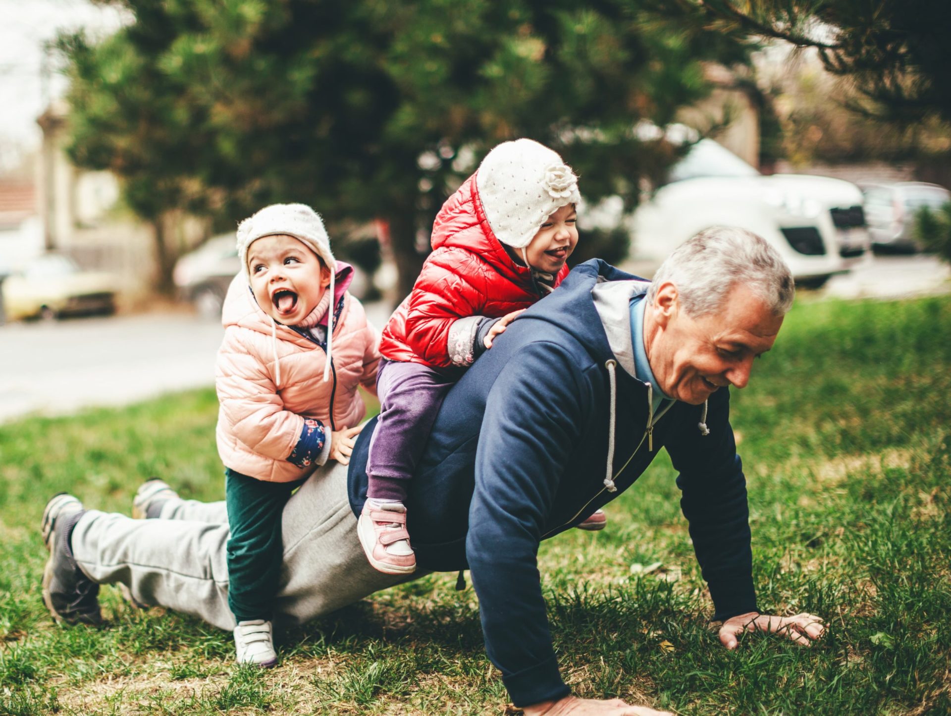 A grandfather does pushups with his two grandchildren on his back