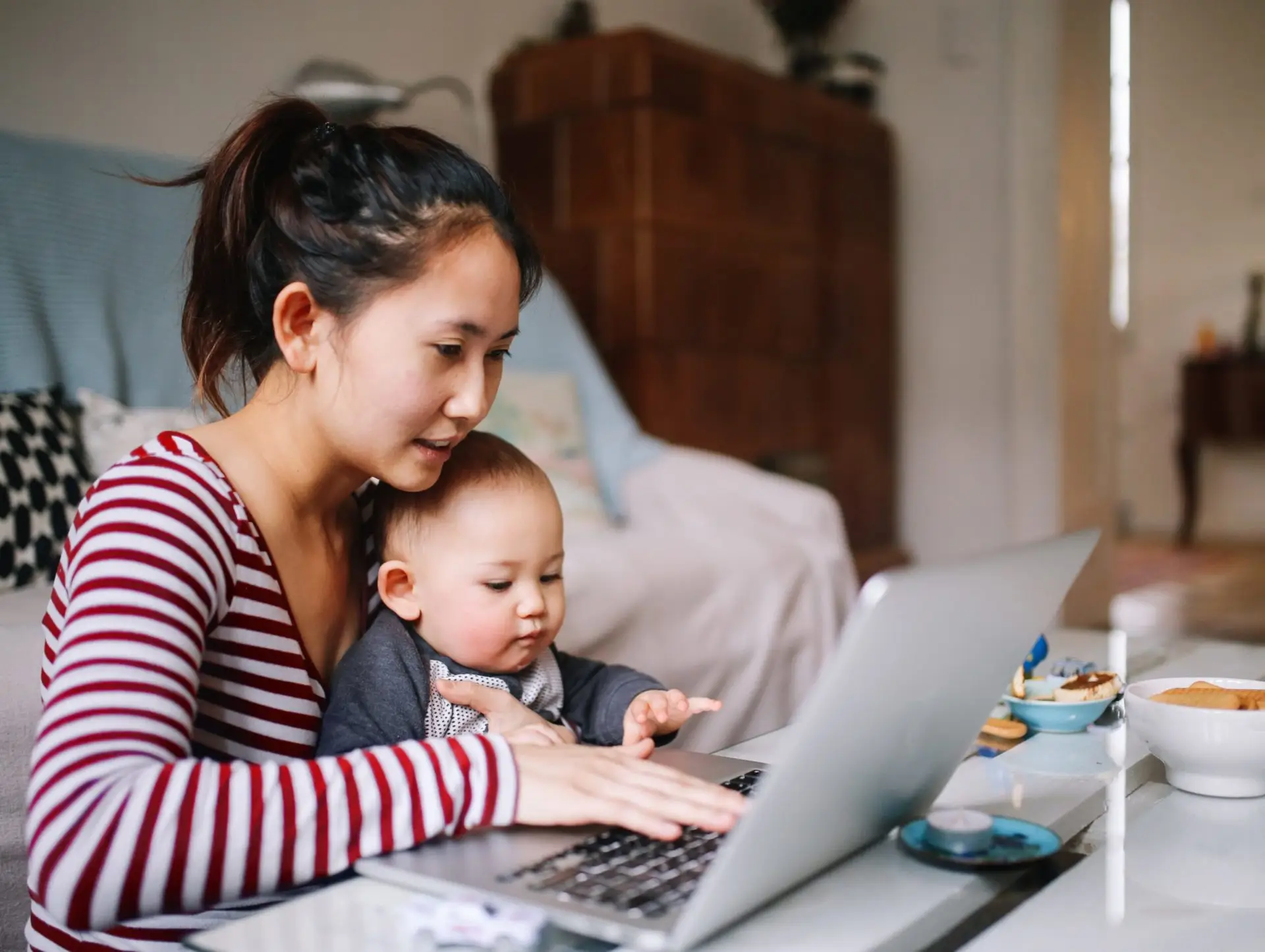 A woman holds her baby on her lap as she works on a laptop