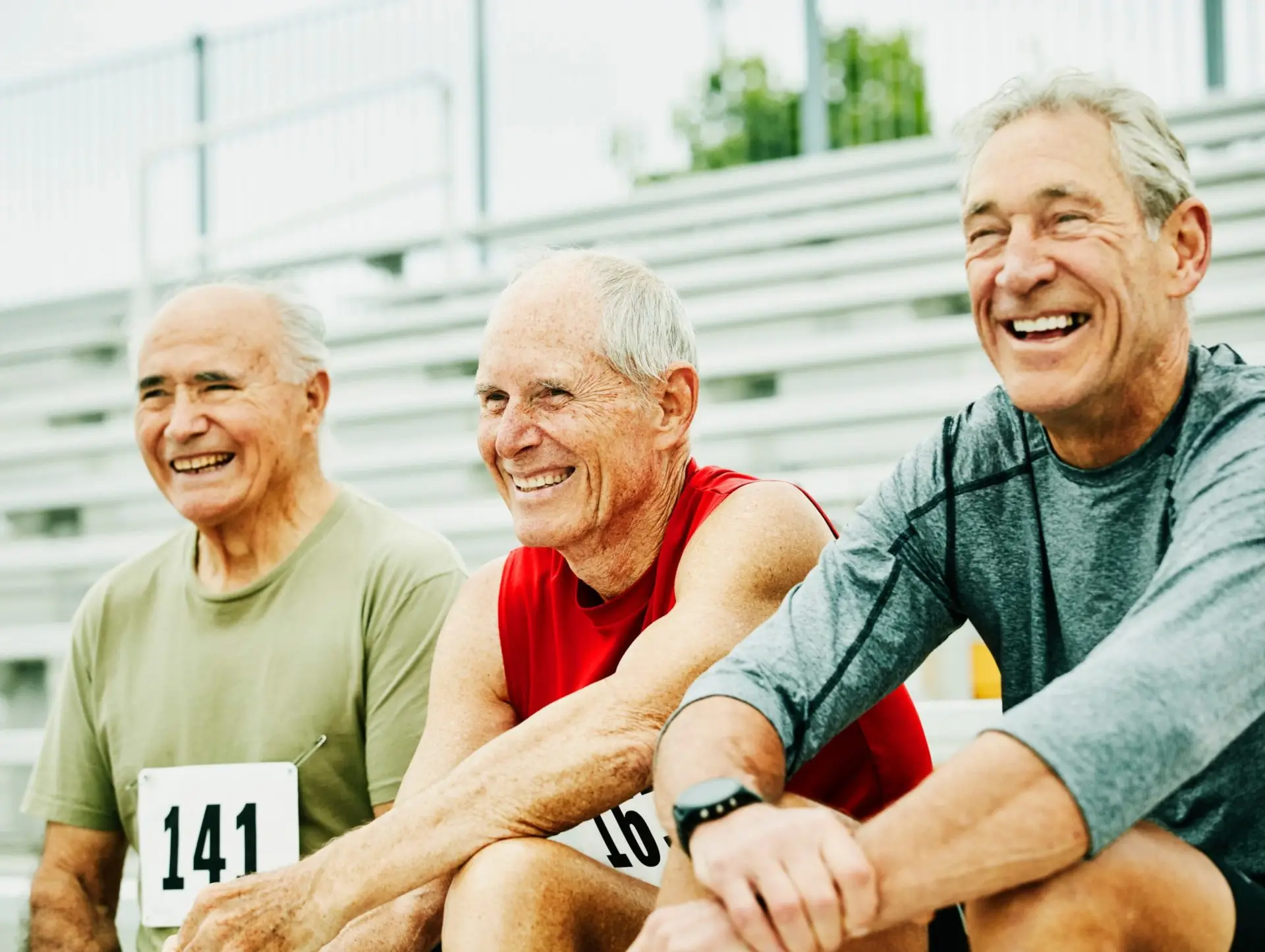 Tres hombres mayores se sientan en las gradas con números de carrera en sus camisetas