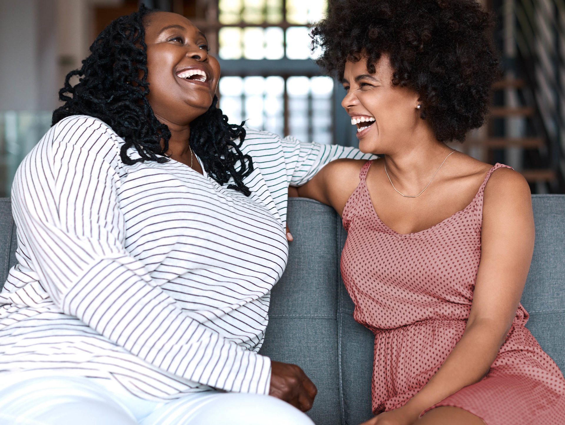 Dos mujeres jóvenes riendo en un sofá.